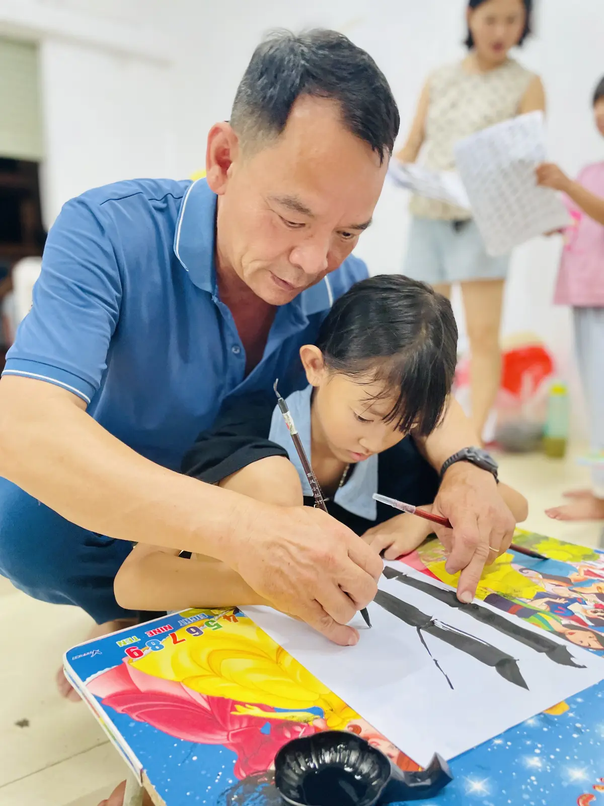 Thầy Lương Mừng cầm tay chỉ nét cho một em nhỏ trong lớp thư pháp