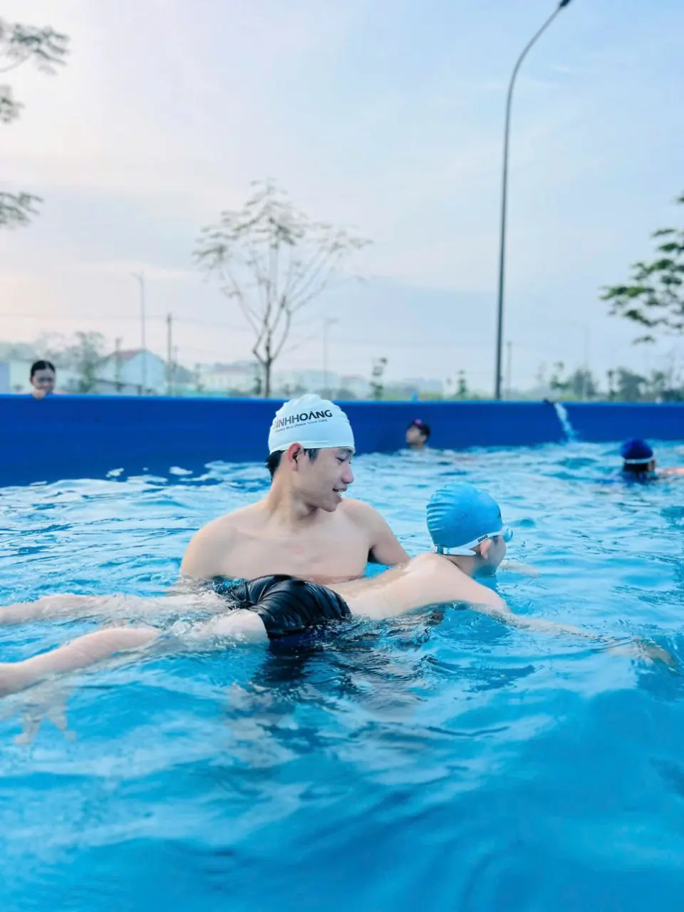 Huấn luyện viên trực tiếp hỗ trợ trẻ tập nổi trong lớp dạy bơi cộng đồng