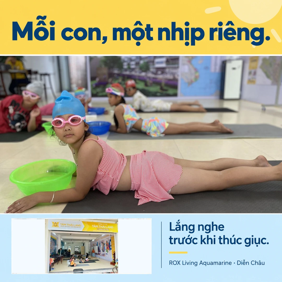 Bạn nhỏ đội mũ bơi xanh, đeo kính hồng trên thảm, ghép cùng không gian sinh hoạt tại văn phòng Tâm Thái Land ở Aquamarine.