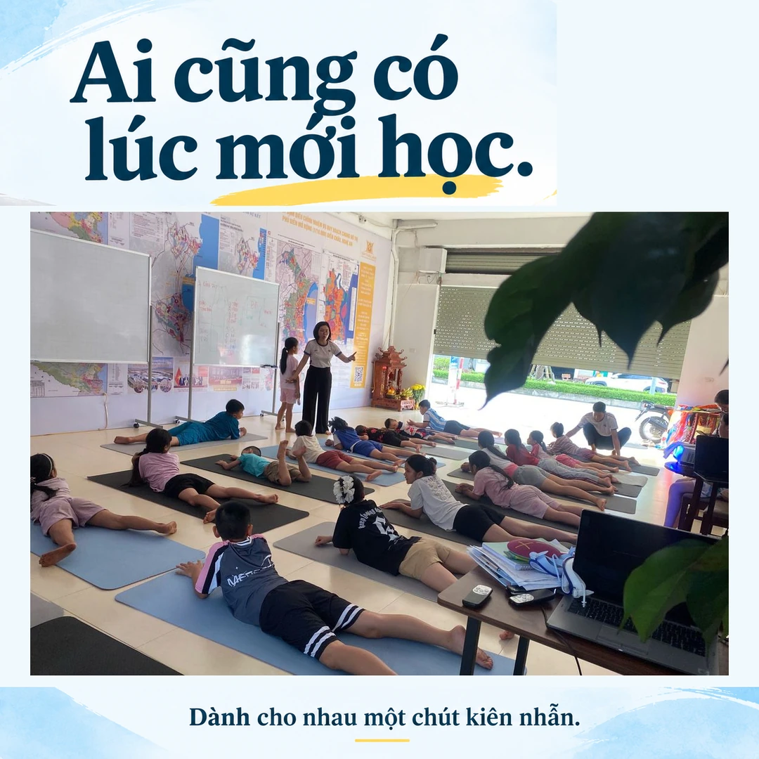 Người lớn và trẻ nhỏ cùng tập trên thảm, phía trước có người đang hướng dẫn trong phòng sinh hoạt Aquamarine.